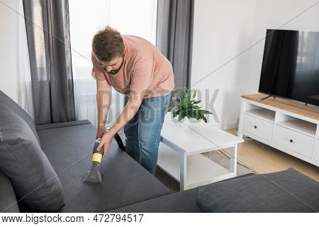 Man Holding Modern Washing Vacuum Cleaner And Cleaning Dirty Sofa With Professionally Detergent. Pro