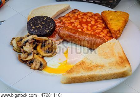 White Board With Full English Breakfast With Bacon, Fried Egg, Beans, Tomato, Roasted Sausage, Black