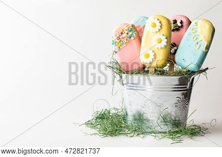 A Tin Pail Filled With Cakesicles Decorated For Spring, Against White.