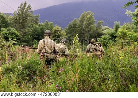 Historical Reconstruction. World War Ii Infantry Division Soldiers Patrol A Site In The Tall Grass. 
