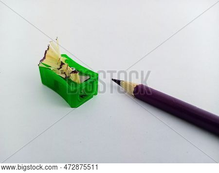 Green Pencil Sharpener With Wood Shavings And A Sharp Purple Pencil Crayon On A White Background