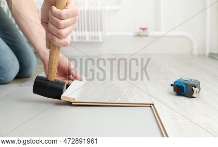 Man Lays A Laminate On The Floor, Hammering It With A Rubber Mallet. Repair And Decoration Of Premis
