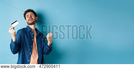 Happy And Satisfied Young Man Dancing With Plastic Credit Card, Fist Pump And Smile, Standing On Blu