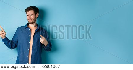 Skeptical Young Man Pointing And Looking Left With Disappointment, Cringe From Something Bad, Standi