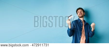 Happy And Satisfied Young Man Dancing With Plastic Credit Card, Fist Pump And Smile, Standing On Blu