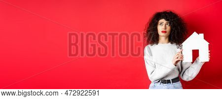 Real Estate. Sad Woman Thinking Of Buying Own House, Showing Paper Home Cutout And Looking Up With U