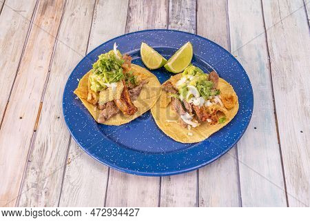 Fusion Tacos With Corn Tortillas, Guacamole, Onion, Meat And Torreznos With Parsley On A Blue Plate
