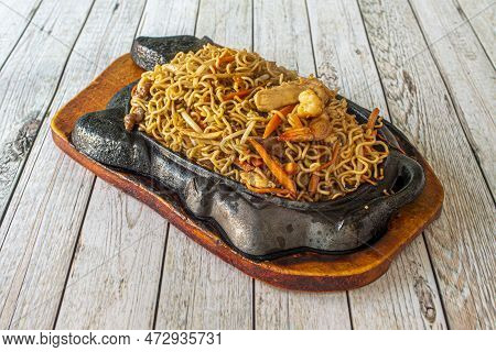 Mixed Chinese Curly Noodles With Sauteed Vegetables, With Meat And With Prawns On Fiery Cast Iron Pl