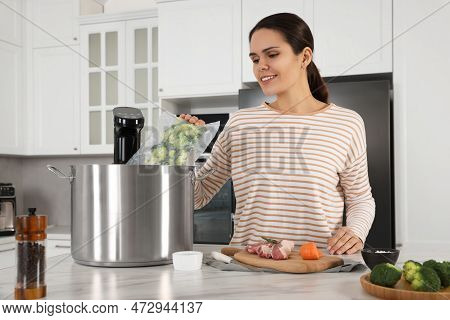 Woman Putting Vacuum Packed Broccoli Into Pot With Sous Vide Cooker In Kitchen. Thermal Immersion Ci