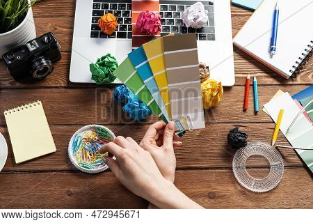 Interior Designer Choosing Colors From Swatches At Wooden Desk. Office Workplace With Laptop And Sta