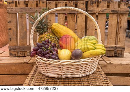 Unvarnished Wicker Basket Filled With Fresh Fruits, Bananas, Mango, Plums And Pineapple