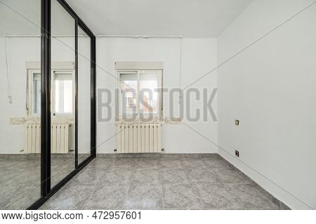 An Empty Bedroom With A Custom Built Closet With Black Metal Edged Sliding Mirror Doors, A Varnished