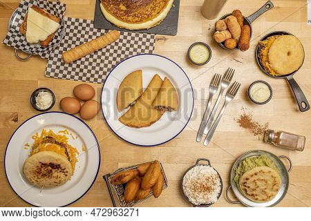 Typical Plates Of Venezuelan Food On Light Wooden Table. Arepas, Cachapas, Tequeños, Corn Empanadas,