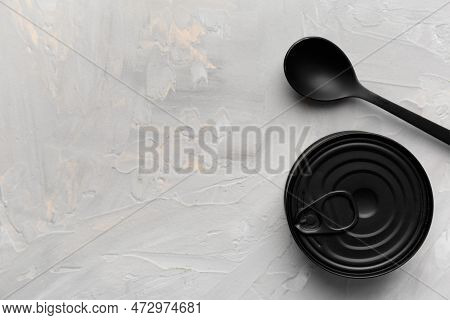 Black Matte Round Closed Tin Can And Black Spoon On Gray Texture Background Top View With Space For 