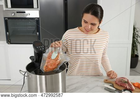 Woman Putting Vacuum Packed Meat Into Pot With Sous Vide Cooker In Kitchen. Thermal Immersion Circul