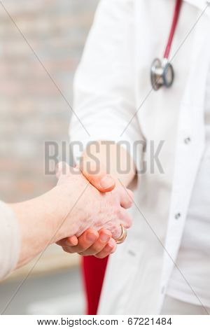 Doctor giving pensioner in surgery comfort and consoling with holding hands 
