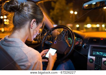 Pretty young woman using her smart phone while driving her car at night