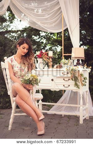 Beautiful Woman Sitting On A White Vintage Chair, Holding A Bouquet, In A Shabby Chic, Vintage Decor