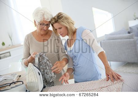 Elderly woman with housekeeper ironing clothes