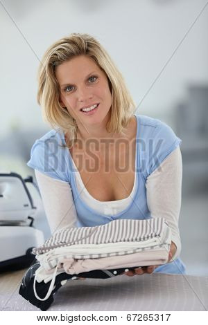Smiling young housekeeper woman holding pile of clothes