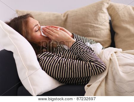 Portrait of a sick woman blowing her nose while sitting on the sofa