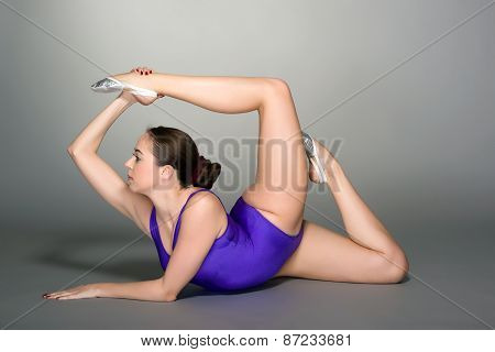 Young Female Contortionist In Purple Leotard On Dark Background