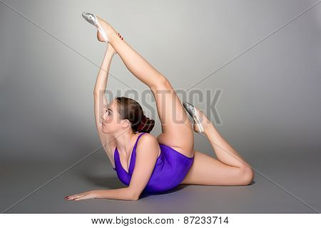 Young Female Contortionist In Purple Leotard On Dark Background