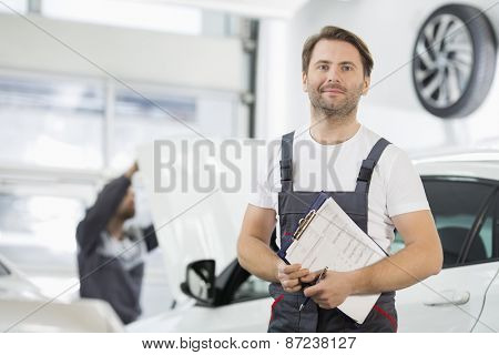 Portrait of confident male maintenance engineer with clipboard in car repair shop