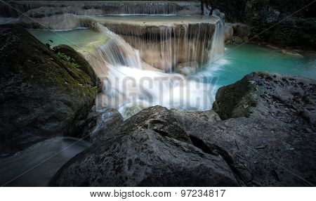 Rapid mountain river stream with cold fresh water running and falling from small waterfalls surrounded by wet stones and rocks