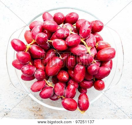 Freshly plucked raw reddish pink date palm fruits with dew drop on it and kept on a bowl
