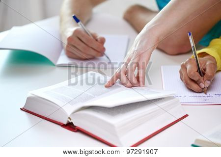 education, people and school concept - close up of students hands with textbooks writing to notebooks at school