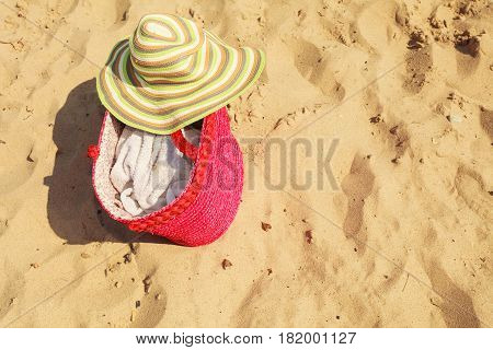 Seasonal specifics. Yellow summer female hat and big red shopper bag lying on sand on beach.