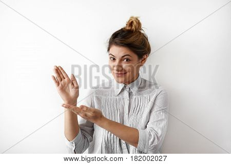 Pretty smiling young woman wearing in striped formal shirt showing something interesting at copy space wall for your information or advertising content. Young Female two hands pointing sideways