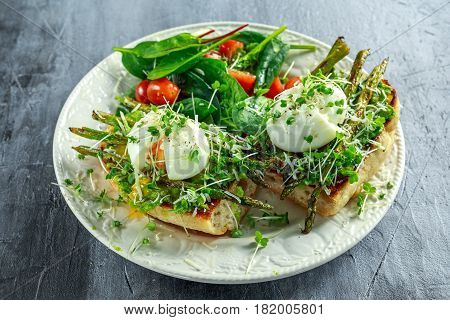 Healthy Breakfast Smashed Avocado, asparagus and poached egg on grilled toasts for breakfast served with salad and plum tomatoes.