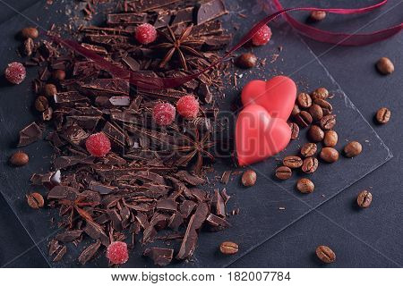 Dark chopping chocolate coffee beans red berries red chocolate with heart shape anise spice on slate board over black textural background. Chocolate dessert confectionery and sweets concept