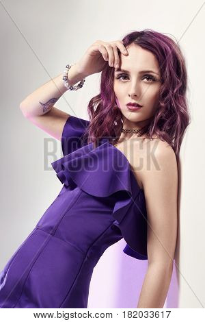 Sexy woman with purple hair and a purple dress posing near the wall. Fashion art portrait of attractive sexy girl