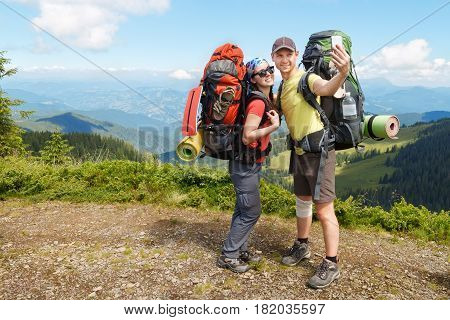 Couple of hikers taking selfie. Tourists woman and man in mountains make selfie uses mobile phone. Mountain selfie in summer. Healthy lifestyle, adventure, tourism, hiking and technology concept