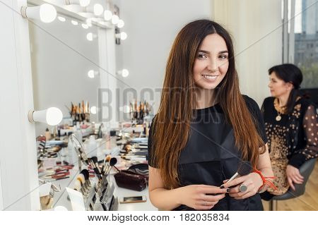 happy young makeup artist holding brush in hands. Visagiste ready to work on a client. Portrait of make-up artist in beauty salon. Real people
