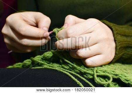 Women's hands knitting green scarf by needles