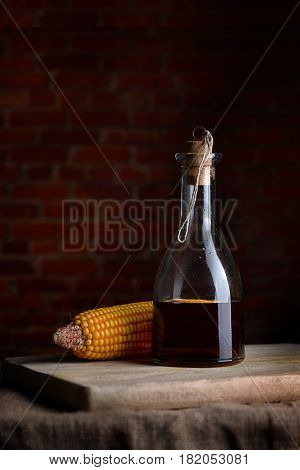 Salad oil in a glass bottle and corn on a background of red block.