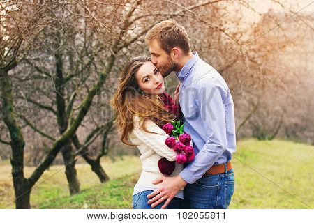 Happy Together. Portrait Of Bearded Hipster Man Kissing His Girlfriend Which Holding Flowers. Beauti