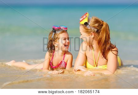 Happy family mother and chid daughter in masks for swimming on the beach in summer