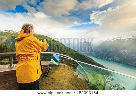 Tourism and travel. Male tourist nature photographer taking photo with camera enjoying Aurland fjord landscape from Stegastein lookout Norway Scandinavia.