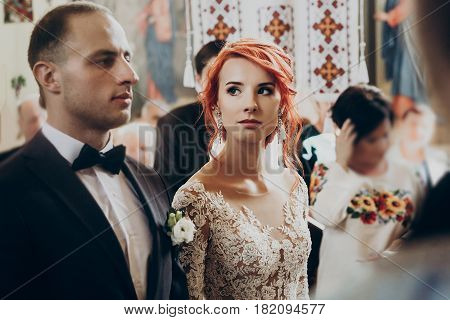 Happy Bride And Stylish Groom Under Crowns And Baptizing During Wedding Ceremony. Wedding Couple At