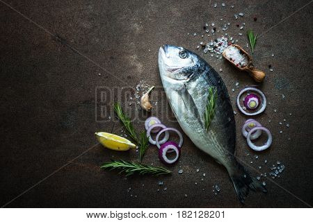 Fresh fish dorado. Dorado and ingredients for cooking at dark rusty table. Top view with copy space.