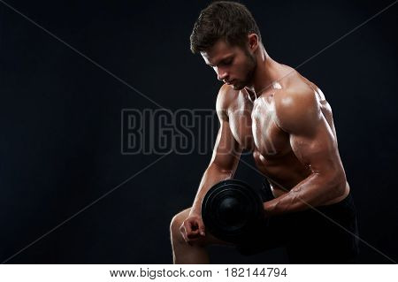Handsome young shirtless athletic man with perfect sexy hot strong body lifting weights exercising with dumbbells on black background copyspace fitness toning shaping healthy lifestyle sport gym.