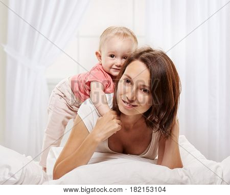 happy family. Mother and baby piggyback playing and smiling on white bed