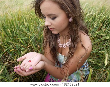 brunette girl in a field with ladybug on her hands