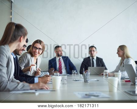 Group of cheerful business people smiling and chatting at meeting table in conference room