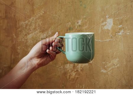 female hand with blue cup with kefir butter milk yogurt or turkish drink ayran natural dairy product on beige wall background. Dieting and healthy eating